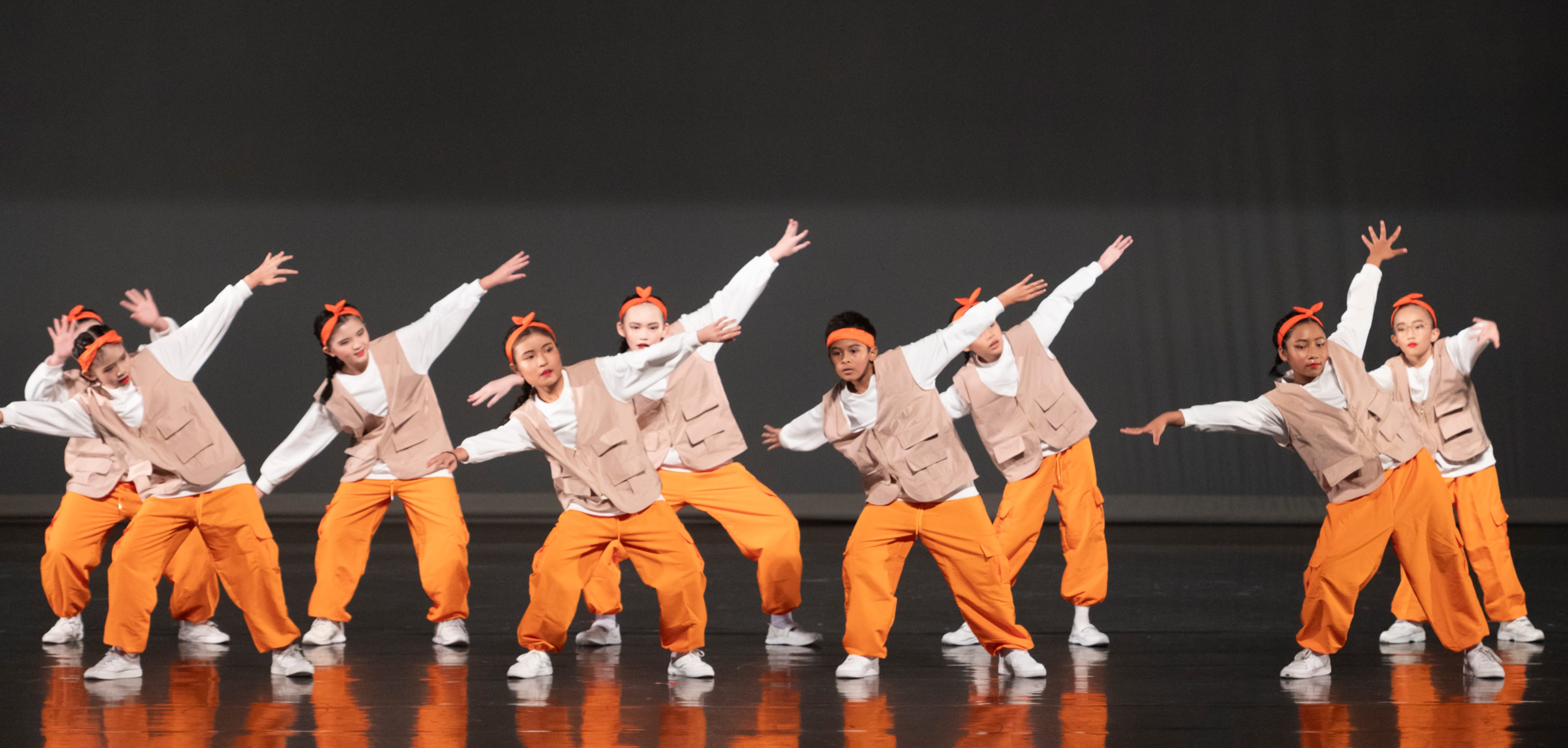 A group of students in orange tracksuits doing a dance move on stage